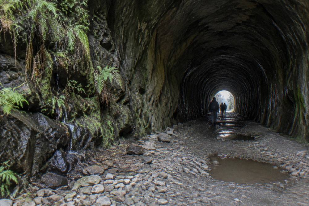 Uneven rocky floor of a long dark railway tunnel lit faintly at the far end