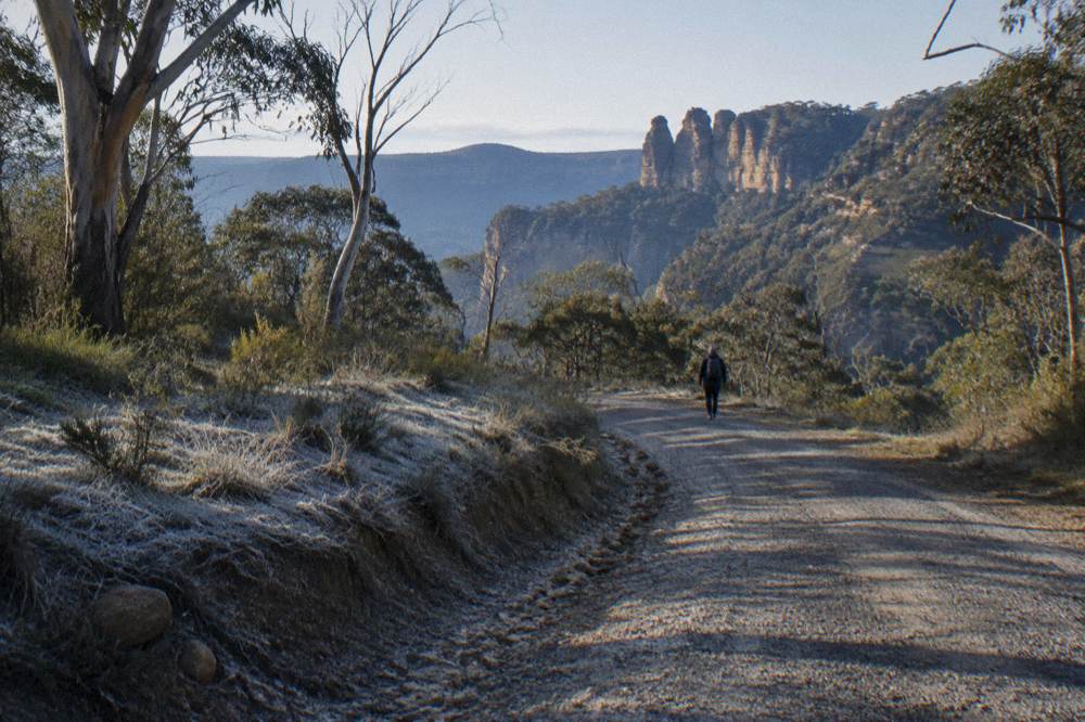 An unsealed gravel road winding through open forest toward distant sandstone pagoda rock formations.