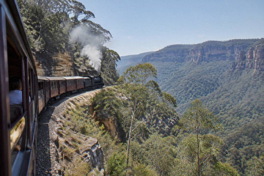 A tourist train winding along a forested ridge above a deep sandstone valley in the Blue Mountains