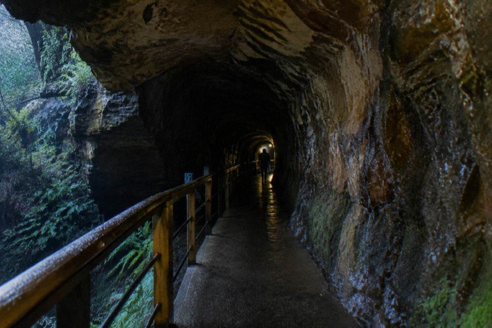 The dark interior of a disused railway tunnel with a walking path and handrail