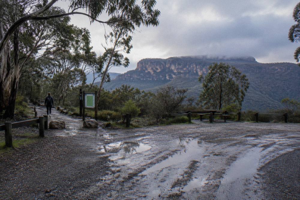 An unsealed gravel road winding through dry eucalypt forest toward a sandstone plateau