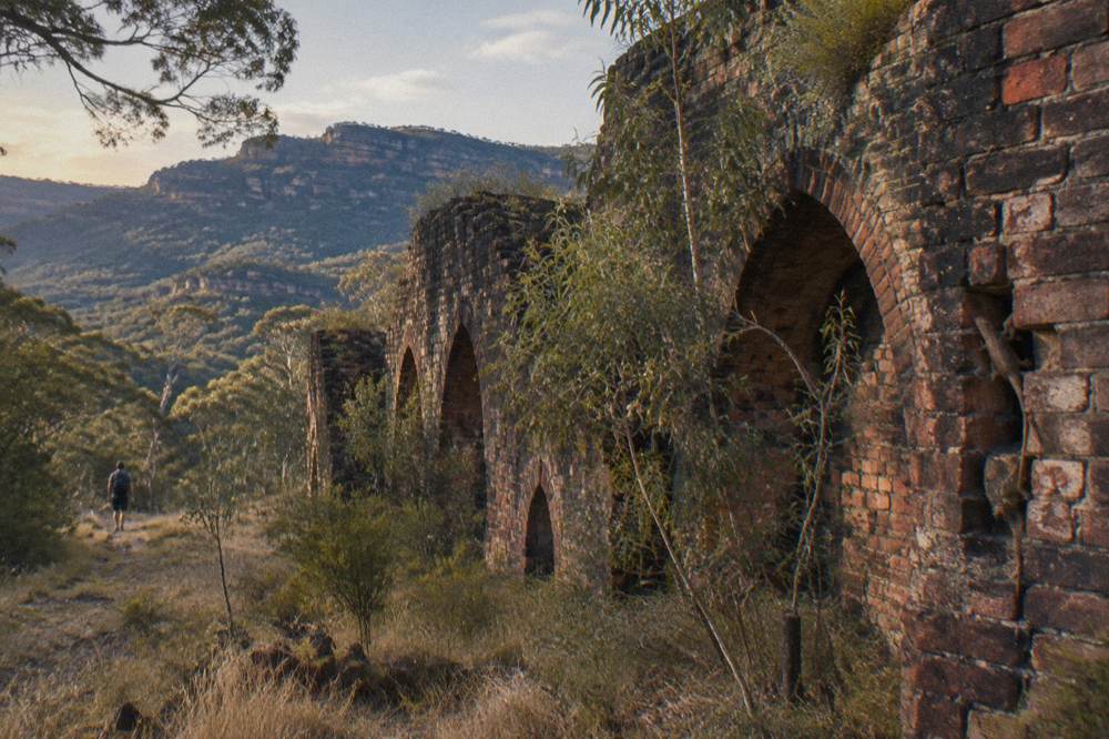 Weathered stone ruins of industrial kilns standing among grass and eucalypts in a valley