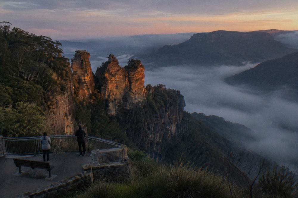 A misty Blue Mountains valley at dusk with layered sandstone cliffs fading into darkness