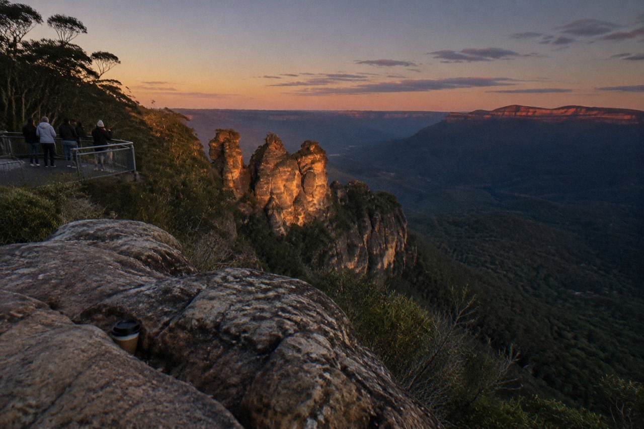 A dark forested valley in the Blue Mountains at dusk with sandstone cliffs catching the last light