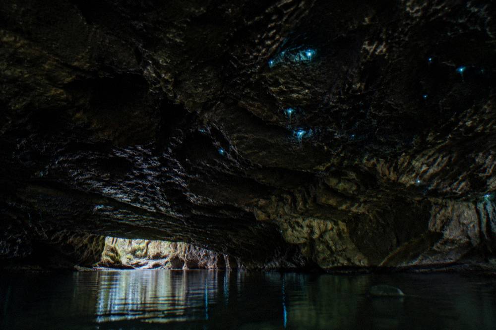 Blue-green points of light scattered across a dark rock ceiling above still water
