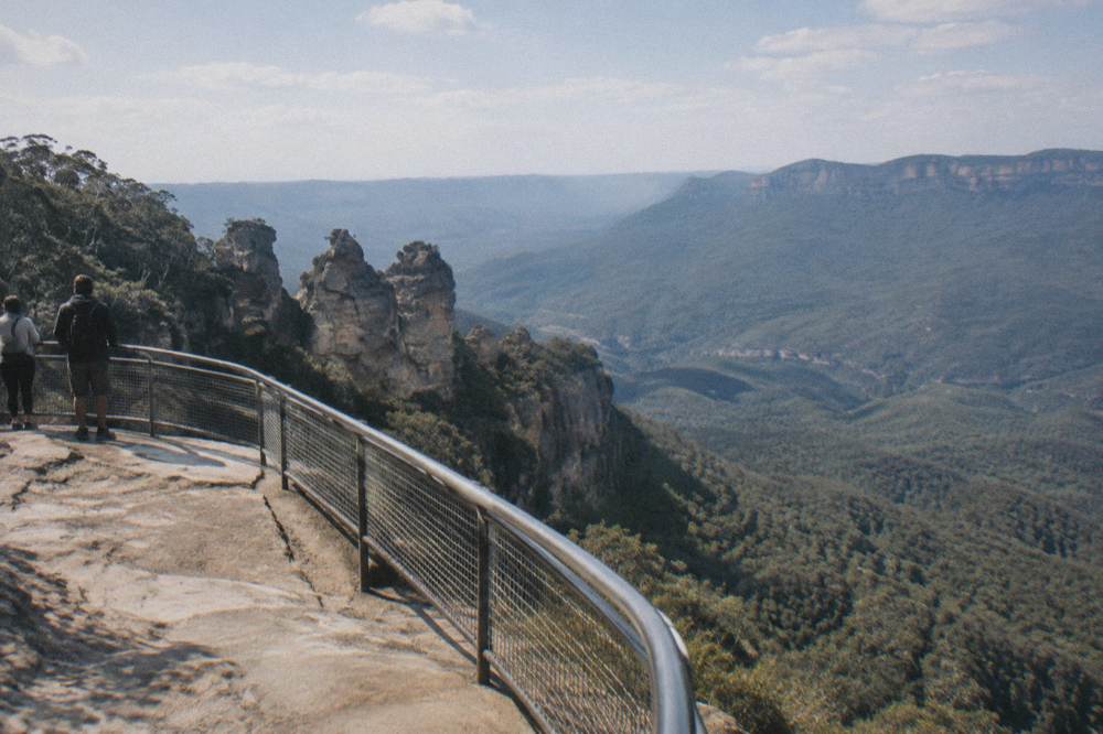 A sandstone cliff lookout above a forested valley with layered ridges fading into haze