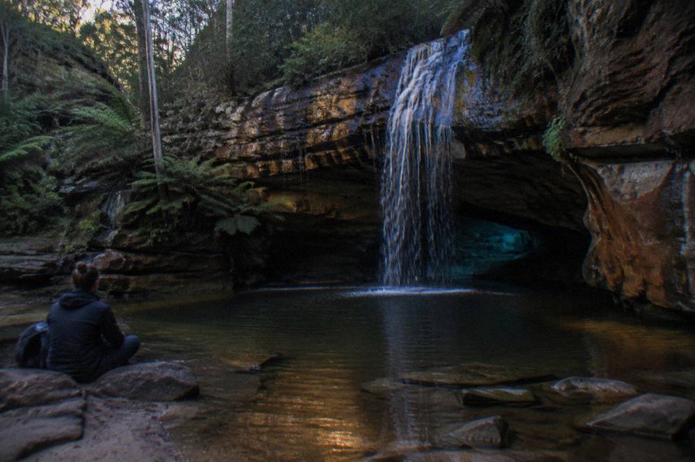 A small cave opening behind a thin waterfall lit faintly in darkness