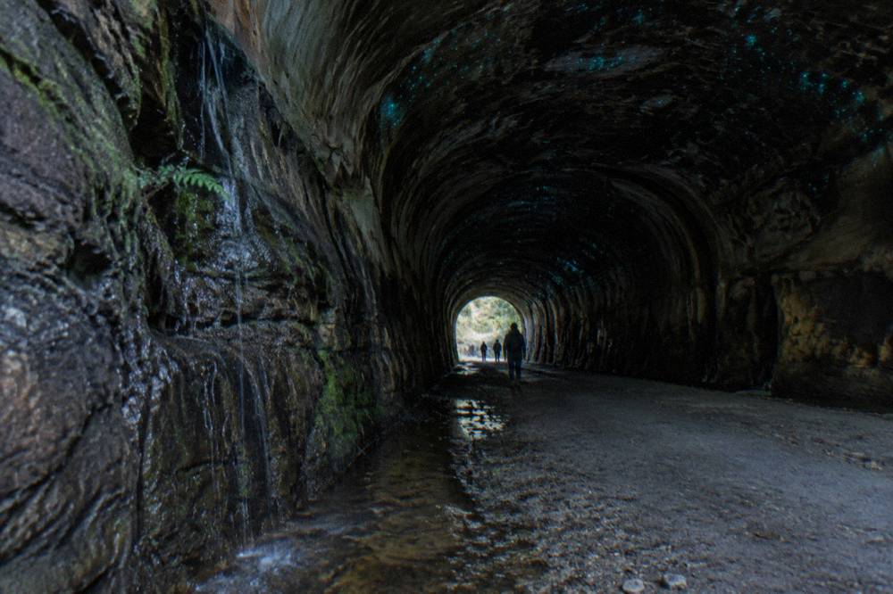 A waterfall trickling over dark cave rock with soft blue-green points of light on the wet ceiling