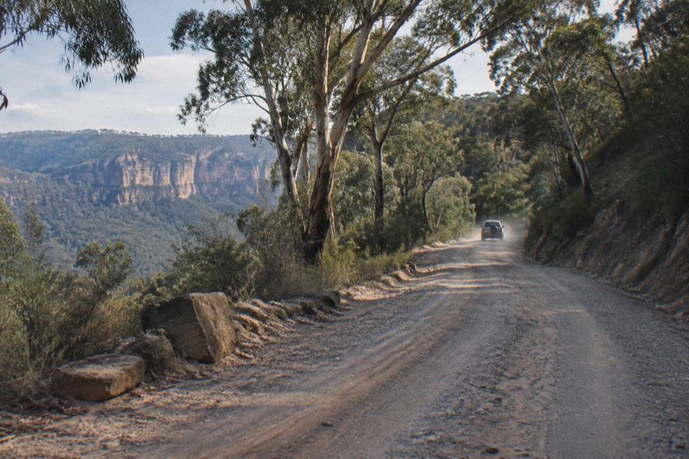 Unsealed gravel road winding through eucalypt forest toward a national park carpark