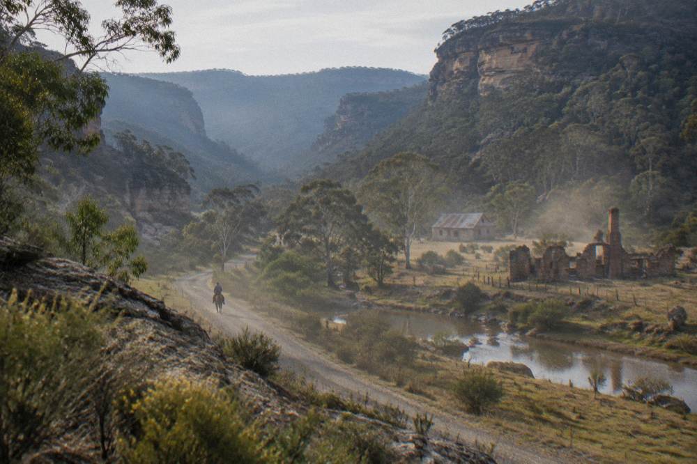 Wide valley floor with forested ridgelines and a narrow gravel road following a river line