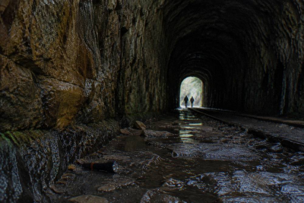 Dark abandoned railway tunnel interior with rough stone walls and a dim far opening