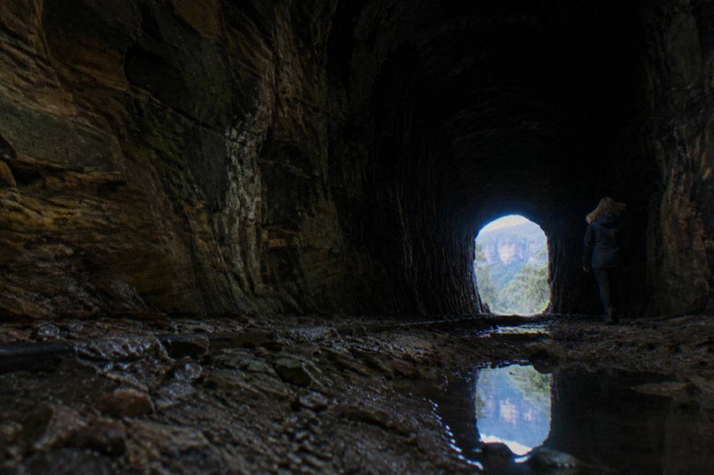A dark railway tunnel interior with a faint glow of distant daylight at the far end
