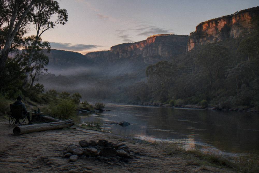 Mist settling over a deep forested valley at dusk with sandstone cliffs catching the last light