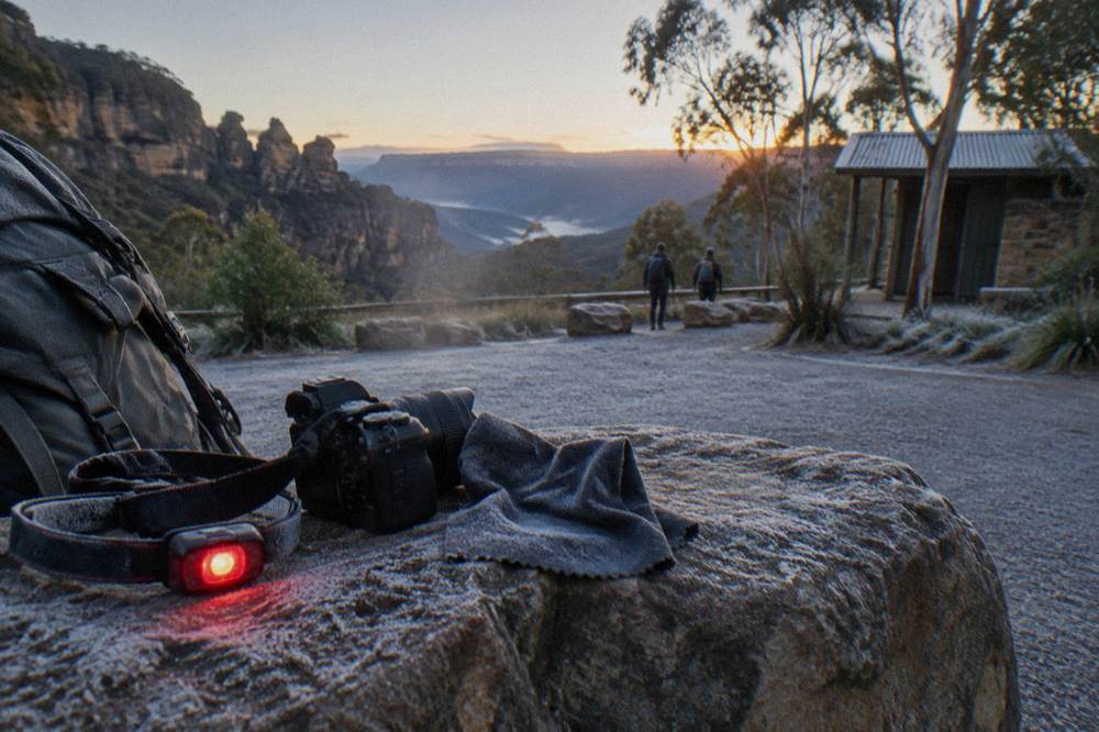 A headlamp with a red light mode resting on a rock beside camera gear