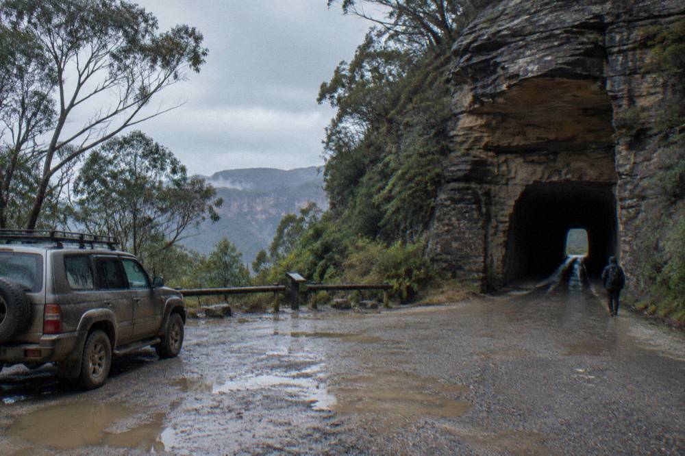 A single-lane rock tunnel on a gravel road with a vehicle waiting at the entrance