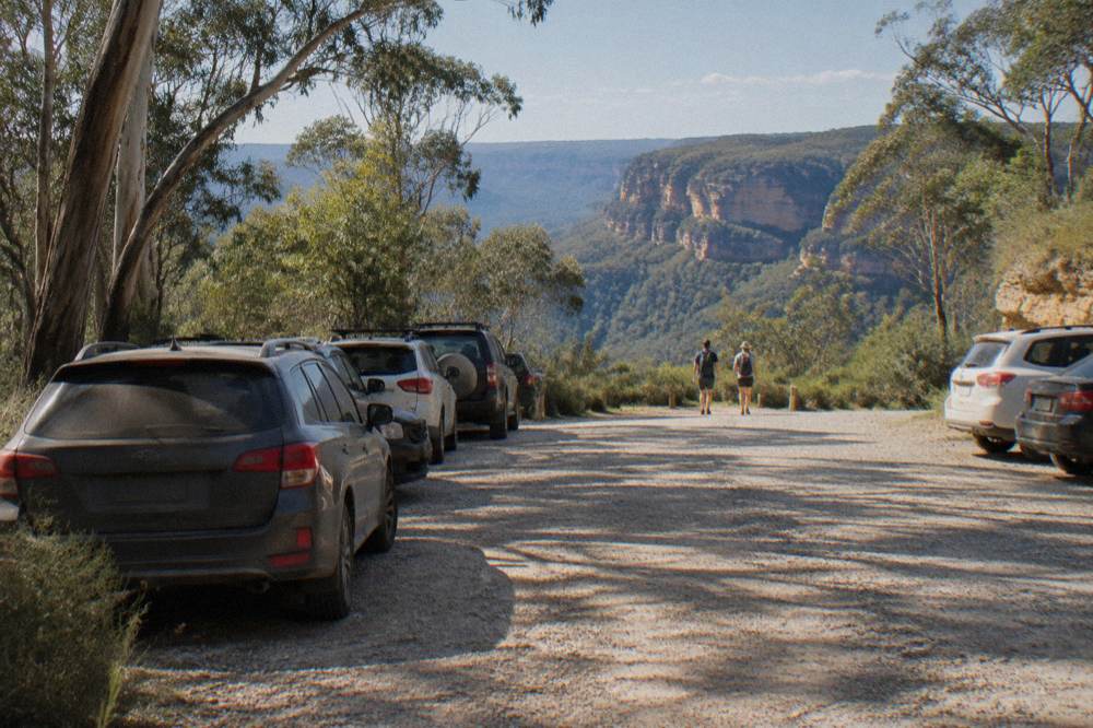 A small gravel carpark at the end of a forest road with a timber bench and a track sign