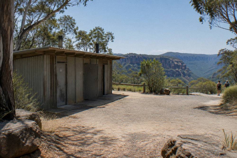 Simple bush toilets and a timber bench at a remote gravel carpark in forest