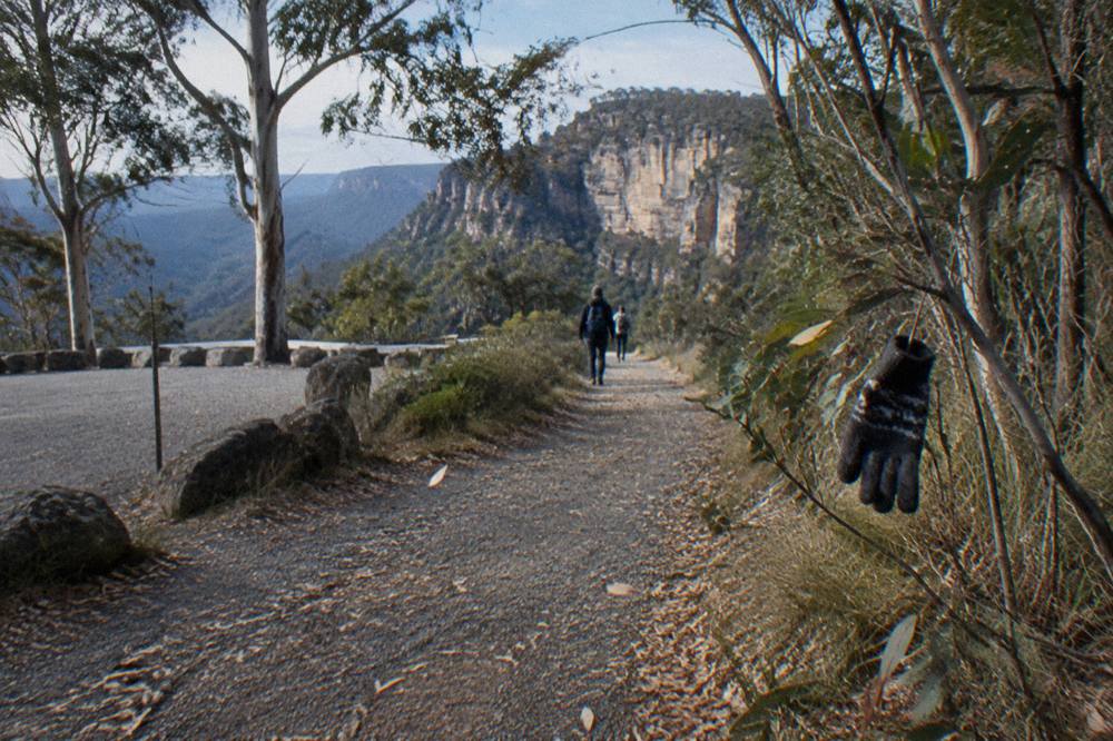 A gravel walking track through dry eucalypt forest heading toward sandstone cliffs