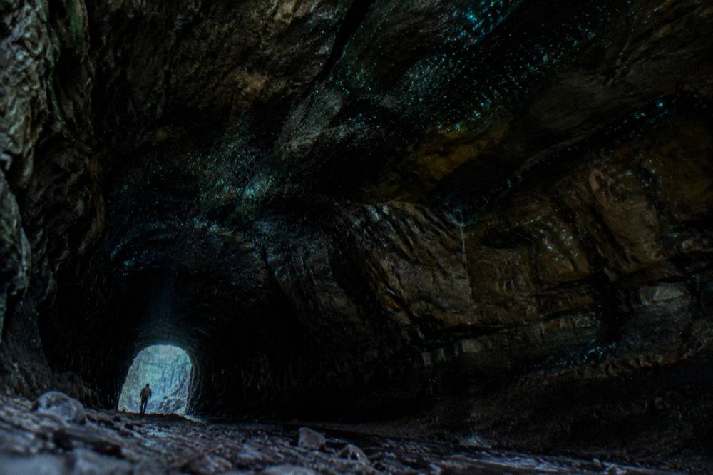 Dark tunnel interior with faint blue-green points of light along the damp rock ceiling