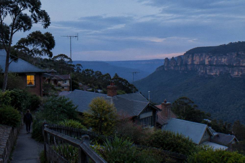 A hillside town at dusk with sandstone cliffs and a valley fading into blue haze
