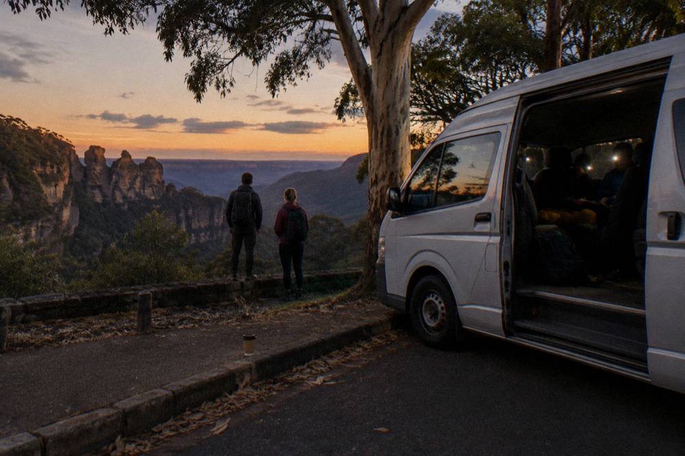 Small van parked on a dark bush road with headlamps glowing near the door