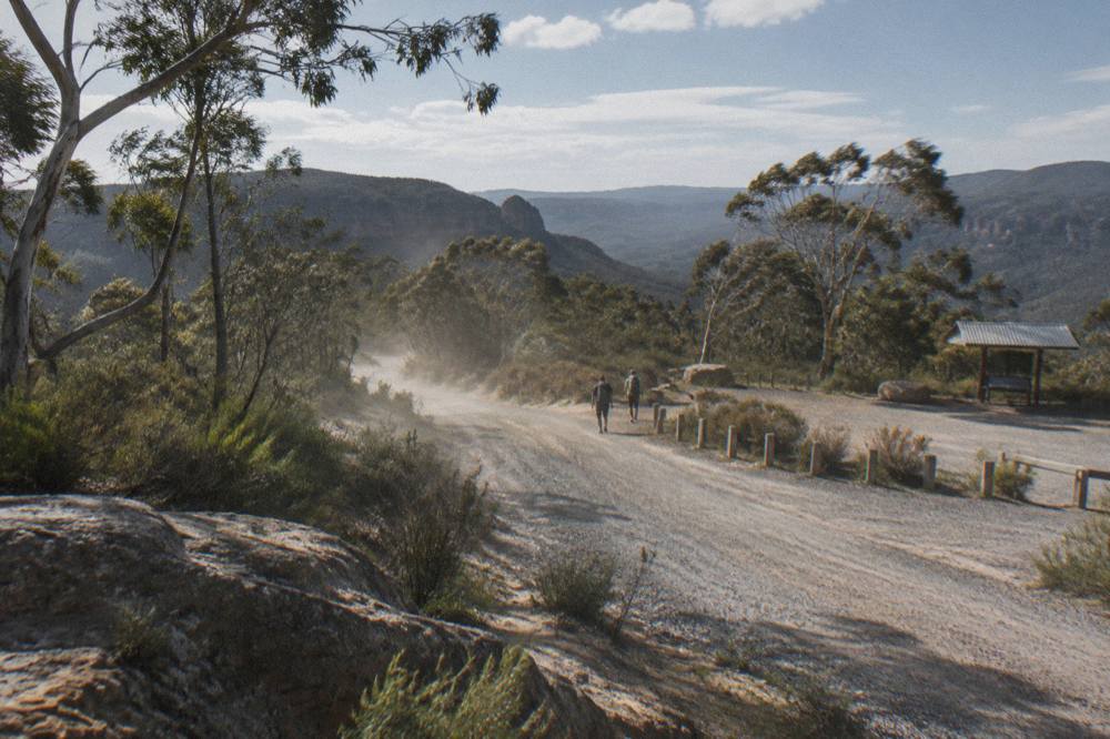 A gravel road winding through dry eucalypt forest toward a low sandstone ridge