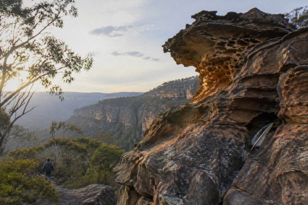 A sandstone pagoda rock formation above a forested valley in late afternoon light