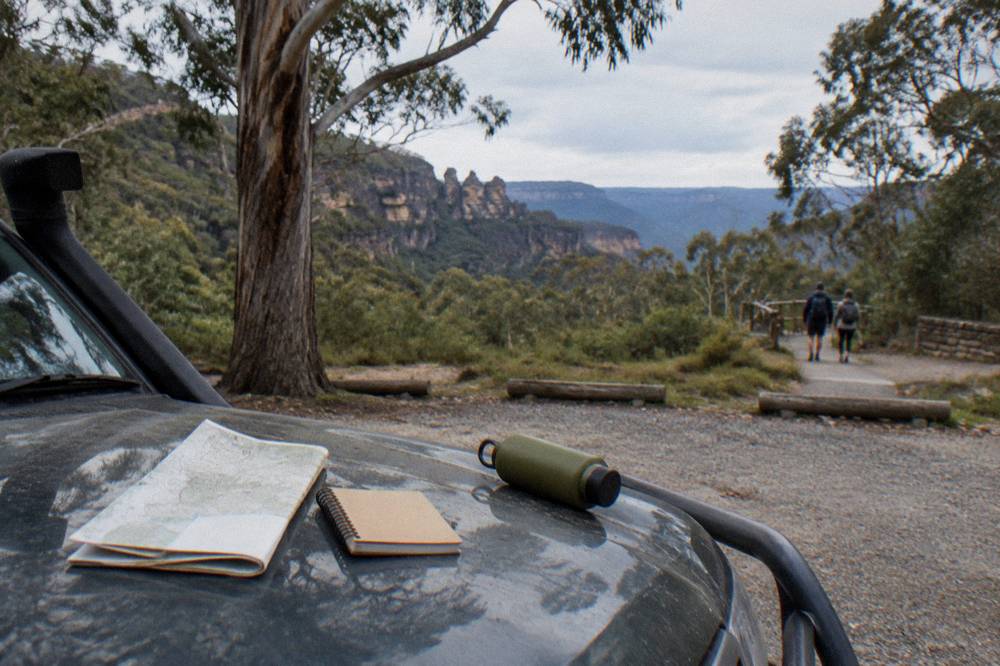 A notebook and map on a car bonnet beside a forest road