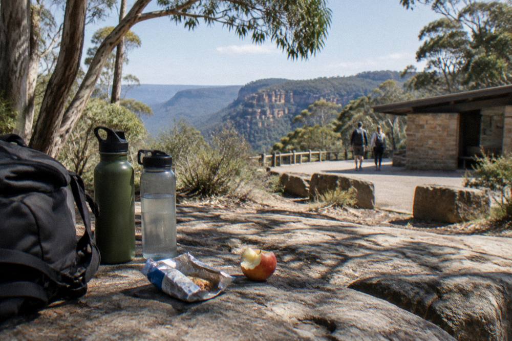 A simple picnic of snacks and water bottles laid out on a timber bench at a trailhead